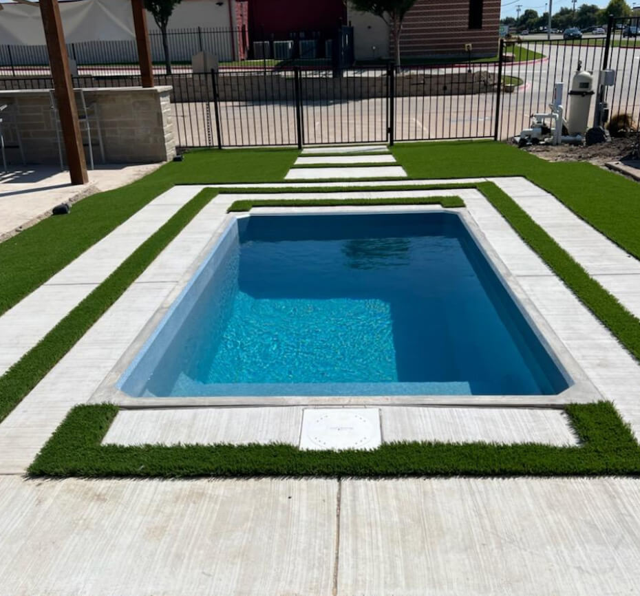 Crystal clear in-ground pool surrounded by concrete walkways and grass in alternating square patterns.
